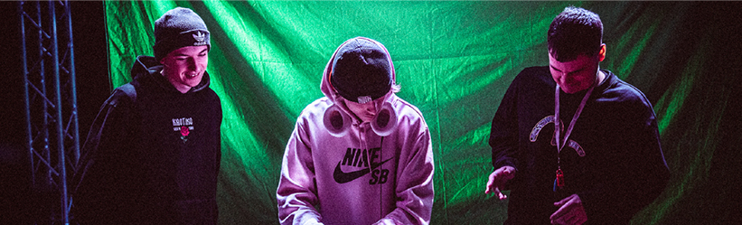 Three young men performing together in front of a green screen.