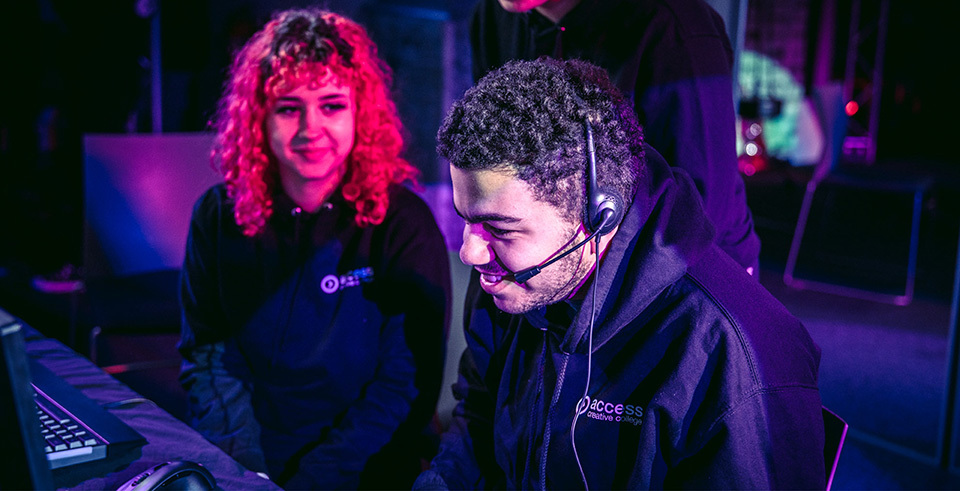 Two students sat at a computer one is wearing a headset