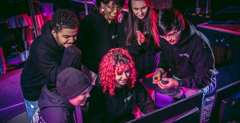 A group of students smiling crowding a computer