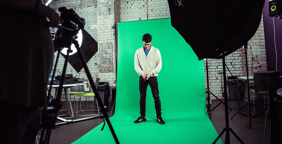 A male stood against a green coloured backdrop in a photoshoot