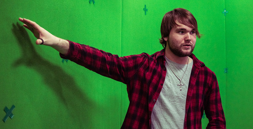 A male gesturing to a green screen backdrop