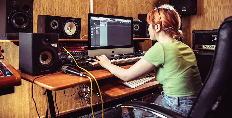 A student sat at an apple mac, the mac has a keyboard attached that they are playing