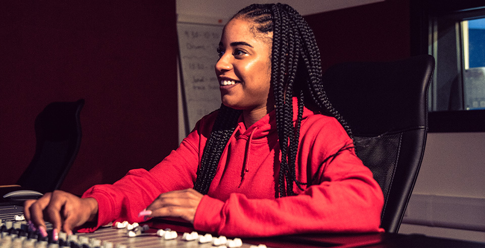 A smiling female working at a music mixing desk