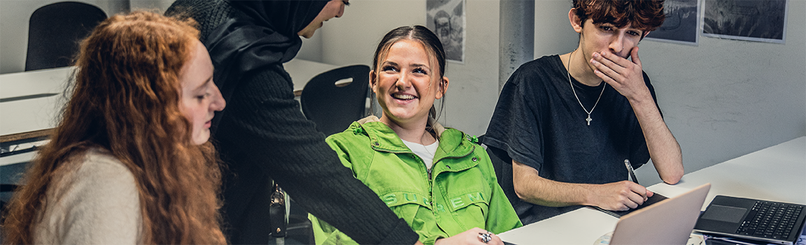 A group of people including a teacher laughing round a laptop