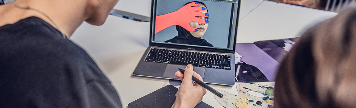 Two people drawing on a tablet and looking at a laptop