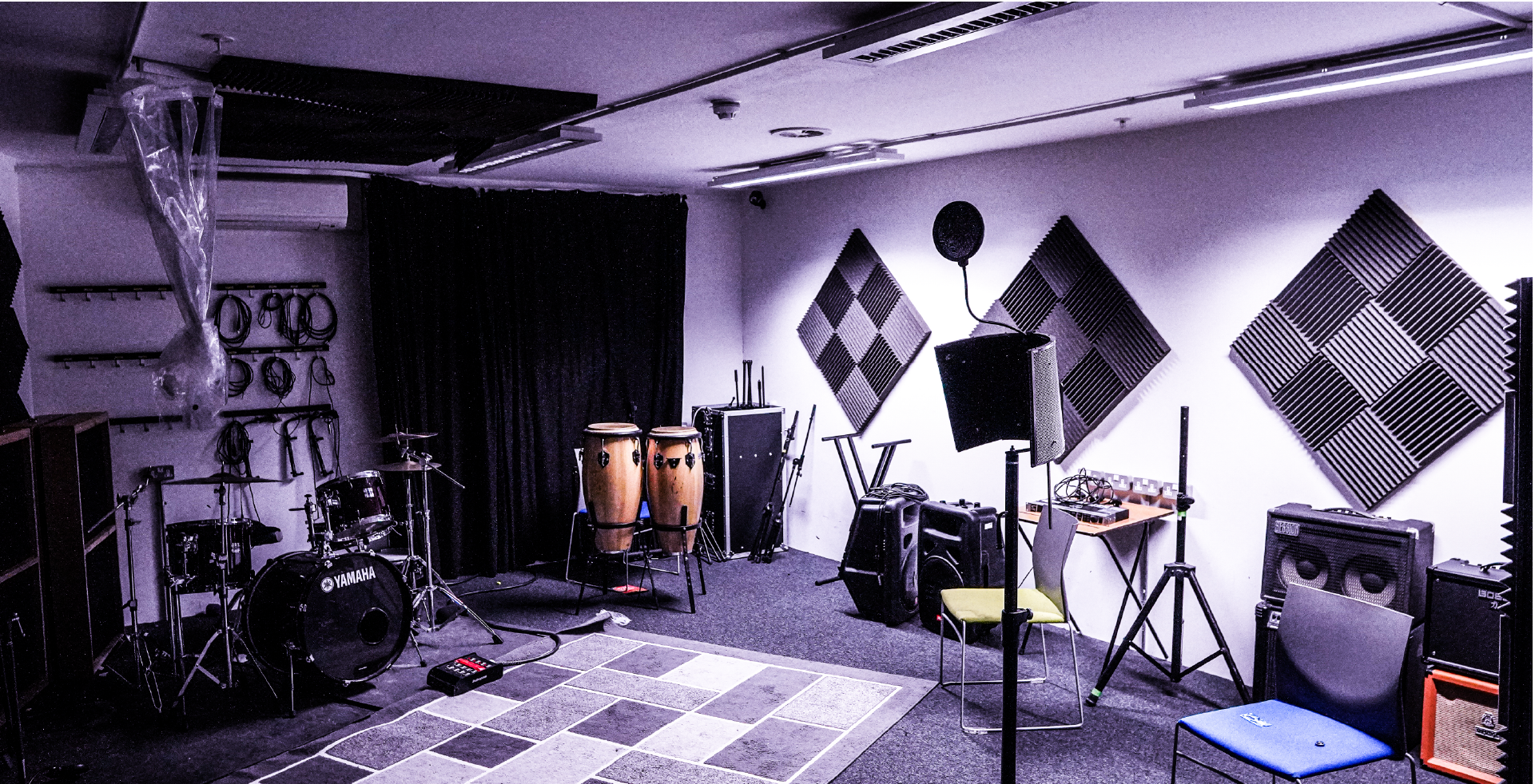 Image of recording studio with music equipment around the room including drums, conga drums and a pop filter