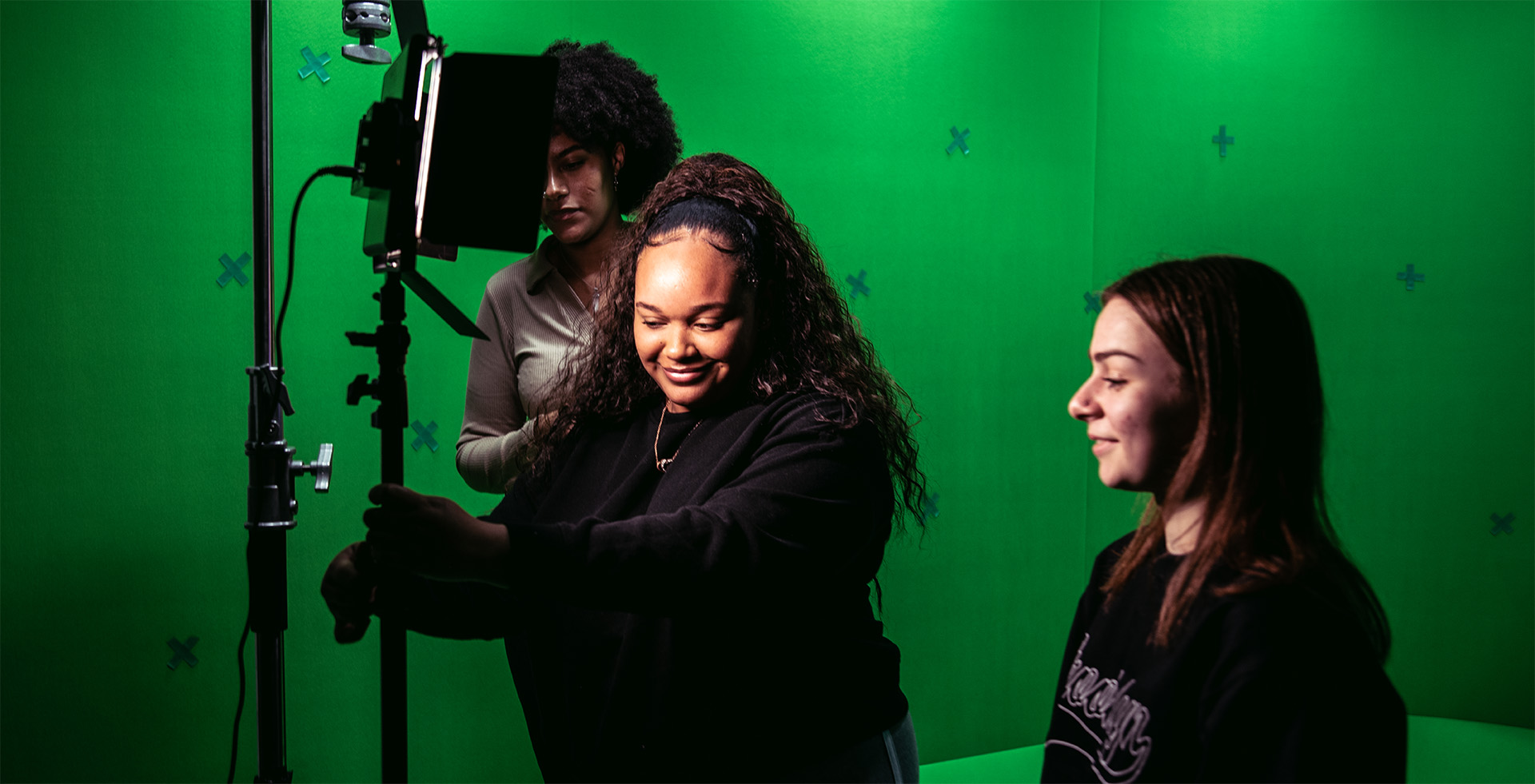 Three people working with lights in a green screen room