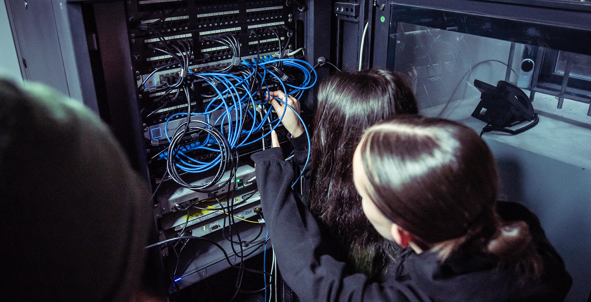 Two females work at a server filled with wiring