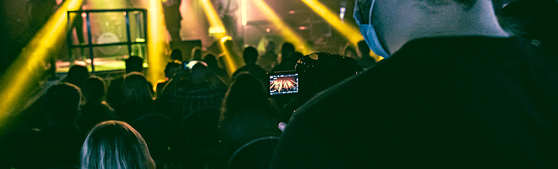 A male filming a band and audience from behind audience