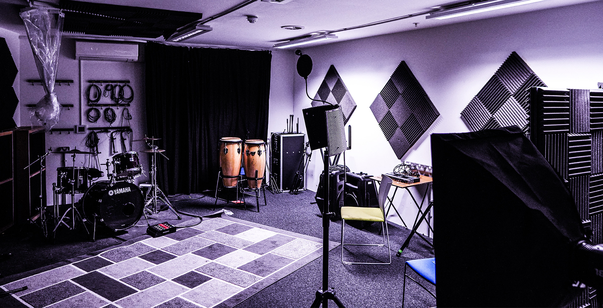 An image of a recording studio with musical equipment around the edge including drums, conga drums and a pop filter