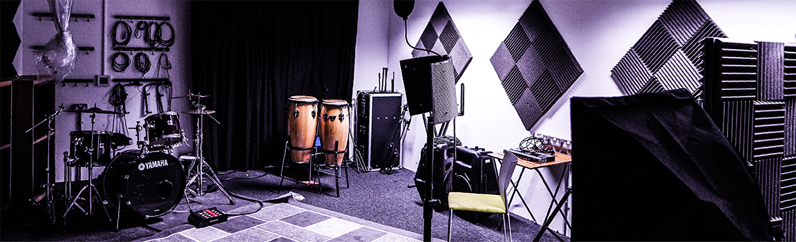 A recording studio with musical equipment around the room including drums, conga drums and a pop filter