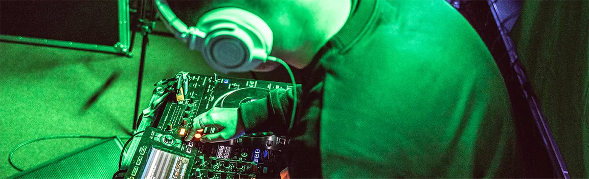 A male wearing over-ear headphones, working at DJ decks