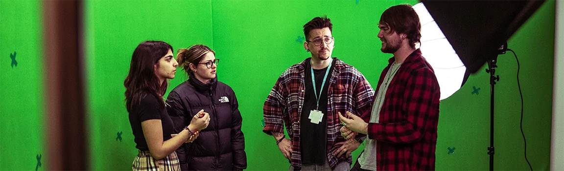 A group of people talking next to studio lights and a green screen background