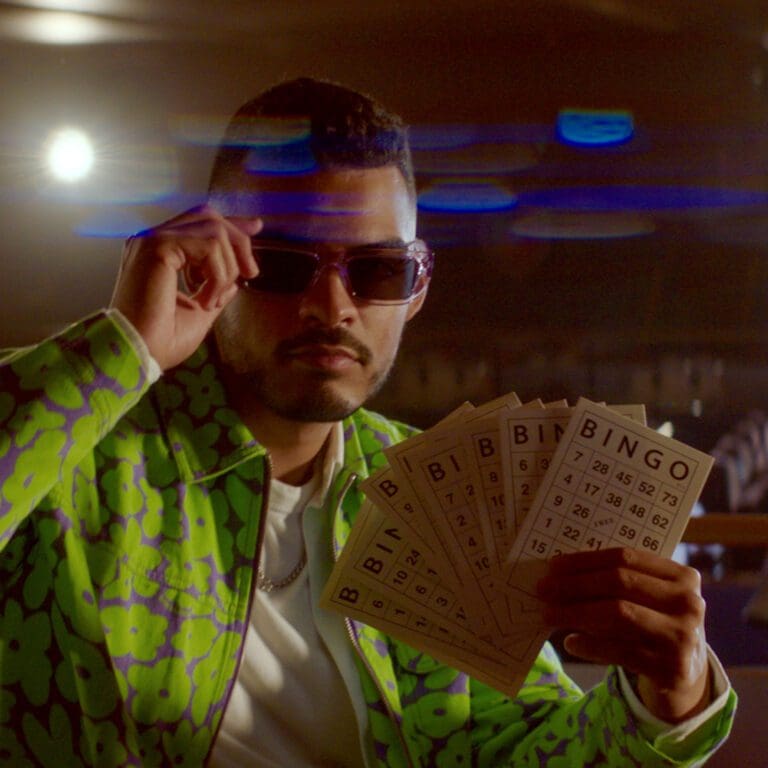 A person wearing a green shirt and sunglasses, holding bingo cards