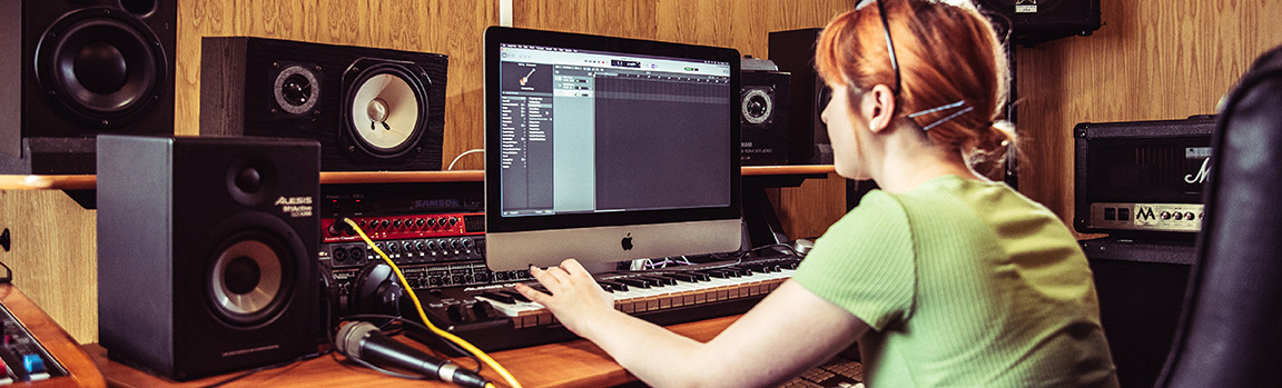 An image of a female working at a computer and MIDI keyboard