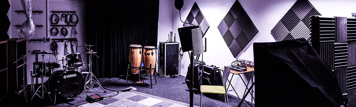 A recording studio with equipment around the room including drums, conga drums and a pop filter