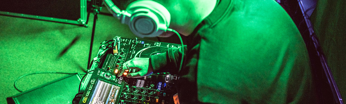 A male in over-ear headphones, working at a DJ deck