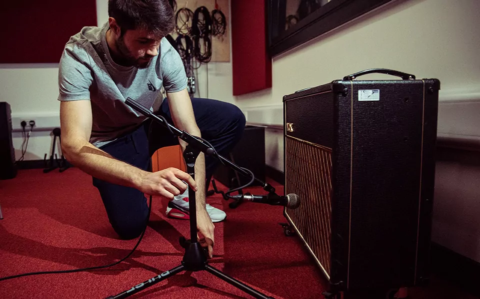 A male adjusts a microphone pointed towards a guitar amp