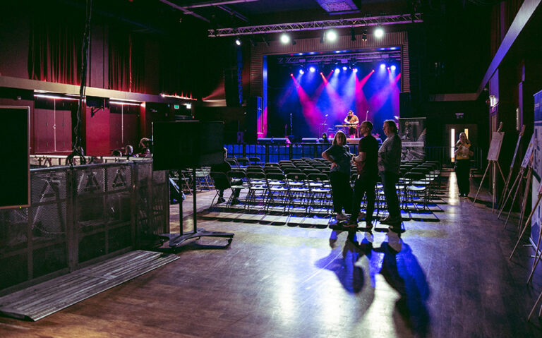 Three people talking in a room filled with empty chairs and a stage