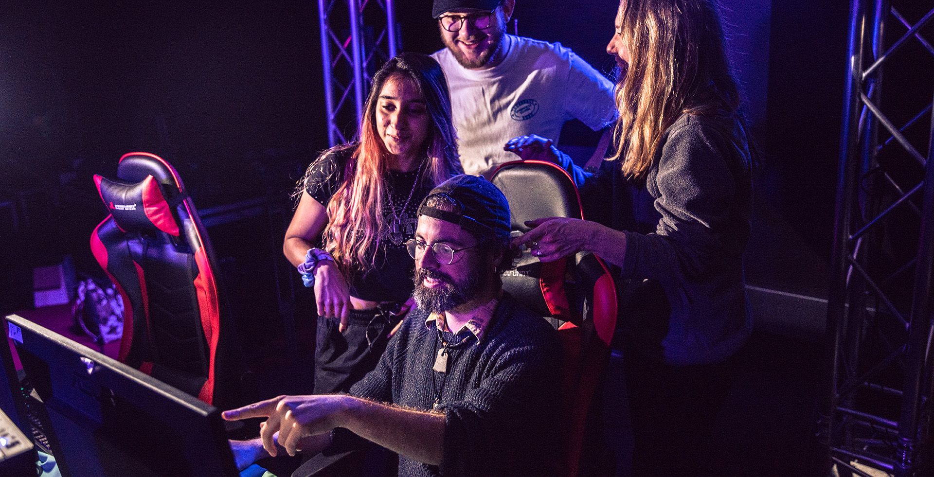 A person sat at a computer, demonstrating something to three people stood behind him