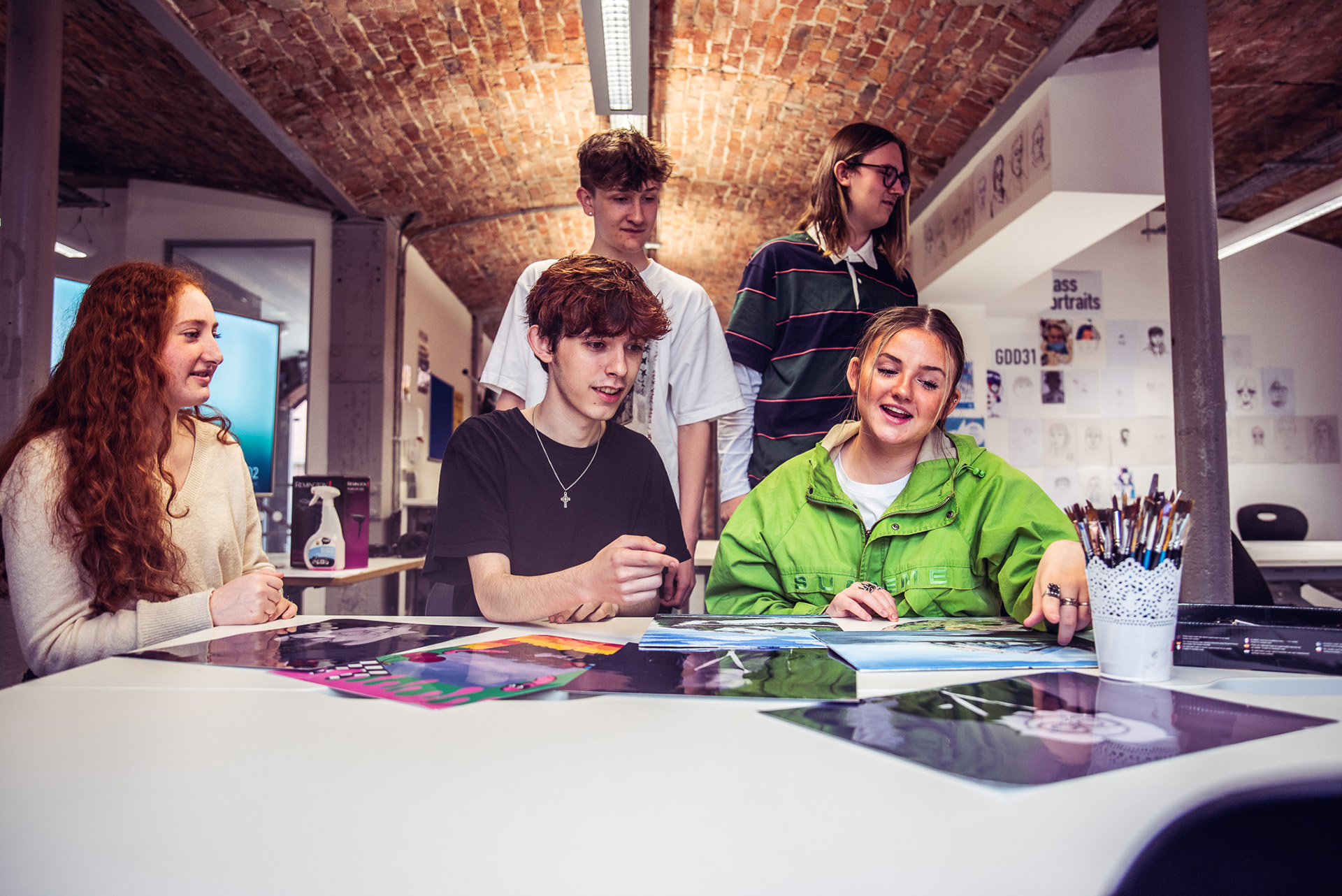 A group of people standing and stood around a table, looking at image print outs