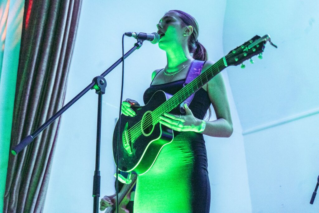 Female Bristol musician singing on stage and playing guitar