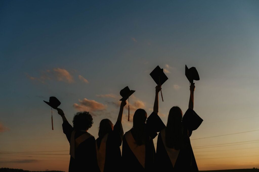 Silhouette of students in graduation gowns, lifting hats in air