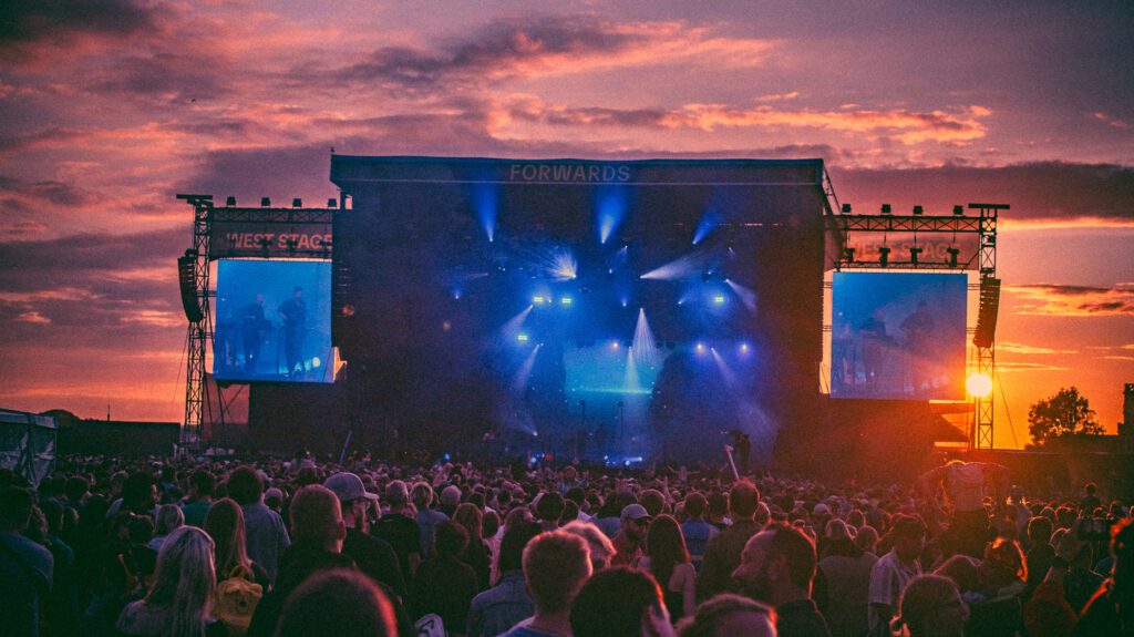 Stage at music festival with crowd cheering on performance